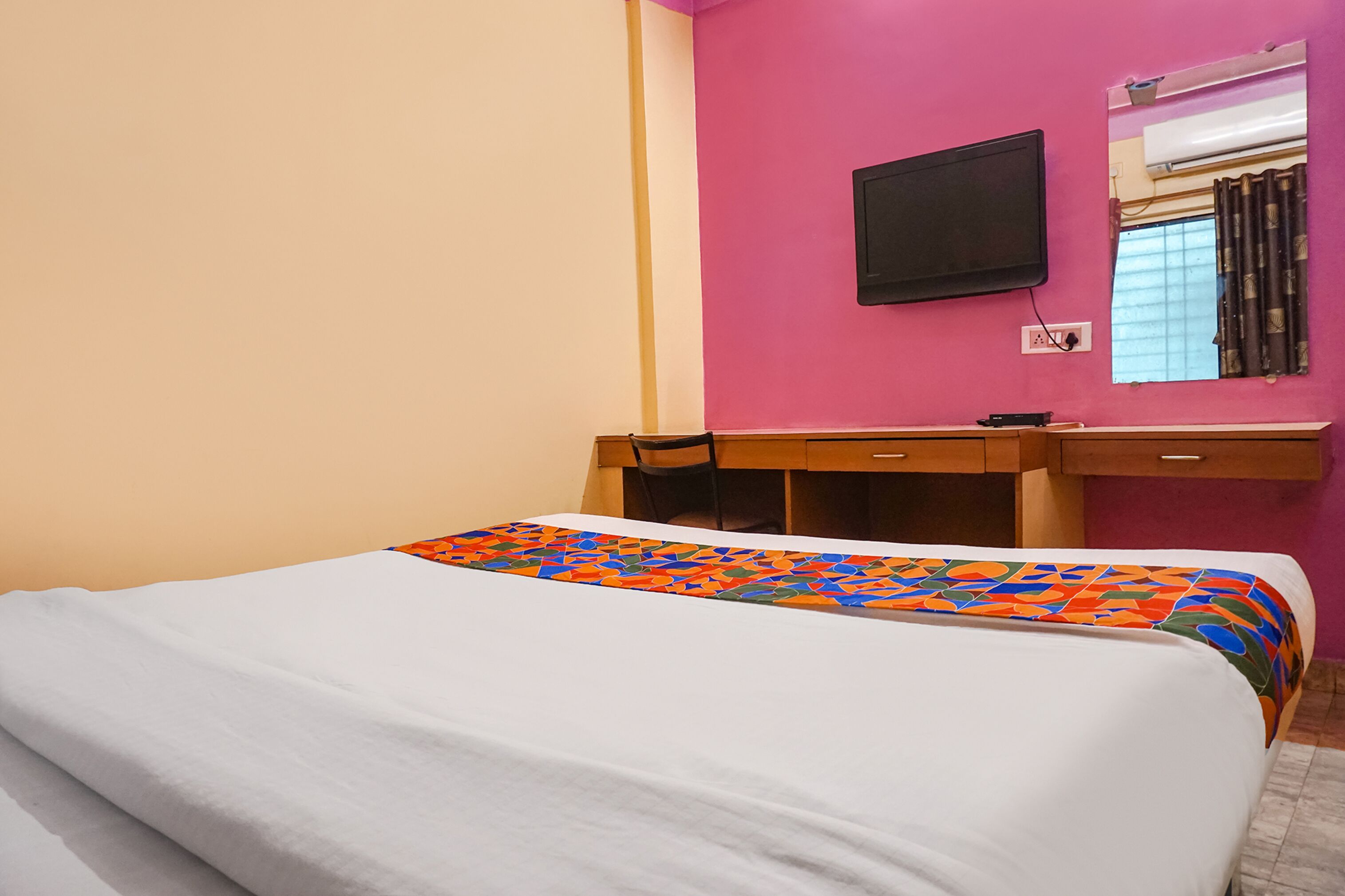 Quarto de hotel com cama, escrivaninha, cadeira, televisão e janela com cortinas.