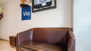 A brown leather sofa in a room with a white wall, a blue sign with 'Via' on it, and a framed picture above the sofa. - Fabexpress Park Residency (Mumbai)