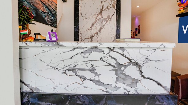A reception desk with a marble top, a framed certificate above it, and a wall with a colorful mural. - Fabexpress Park Residency (Mumbai)
