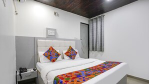 A bedroom with a bed, a bedside table with a phone, and a window with curtains. - Fabexpress Park Residency (Mumbai)