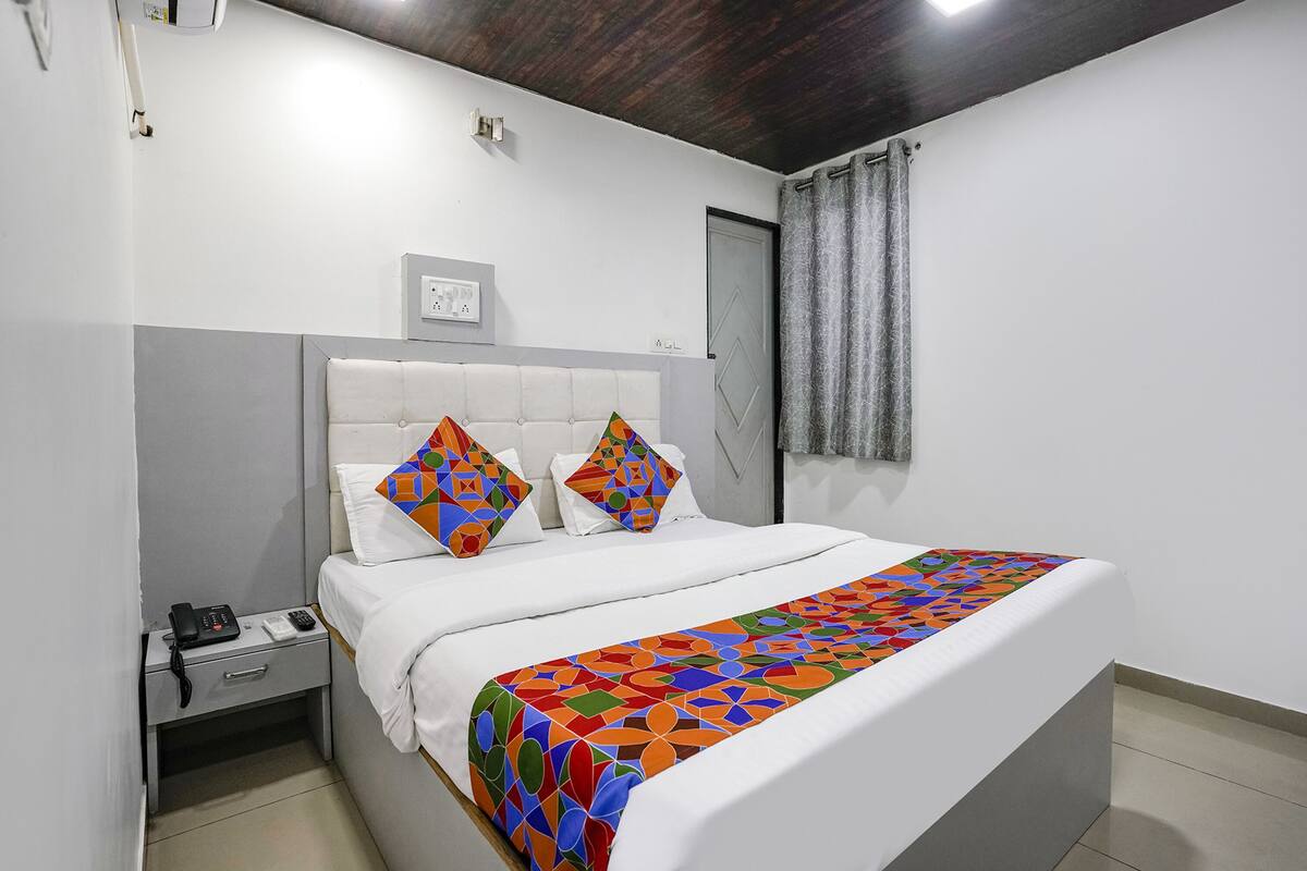 A bedroom with a bed, a bedside table with a phone, and a window with curtains.