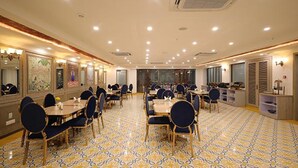 A spacious dining area with multiple tables and chairs, a patterned floor, and a large window providing natural light. - Fabhotel Prime Hampton By Ic'S (Noida)
