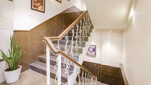 A modern staircase with marble steps and a wooden handrail, flanked by wall-mounted light fixtures and framed artwork. - Fabhotel Springs Lodging (Mumbai)