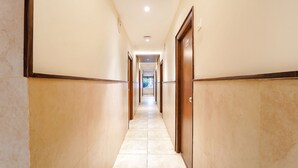 A long, narrow hallway with tiled flooring and wooden doors on both sides. - Fabhotel Karpagam (Coimbatore)