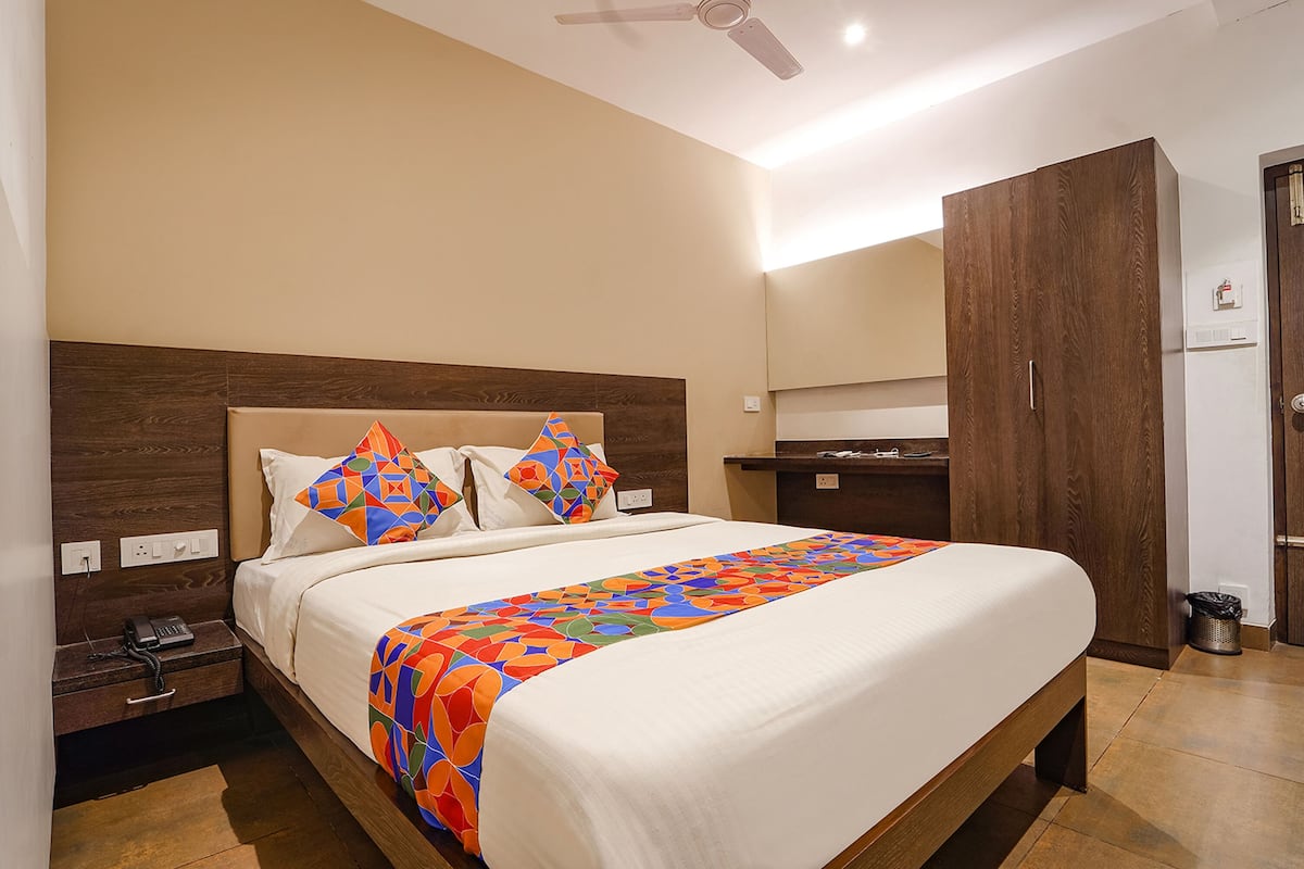 Habitación de hotel con una cama grande, cabecera de madera y colcha colorida. Se observa un mesita de noche con un teléfono y un cesto de basura.