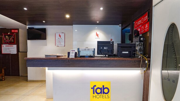 A hotel reception desk with a logo, a flat-screen TV, a printer, and a sign indicating room rates. - Fabhotel Karpagam (Coimbatore)