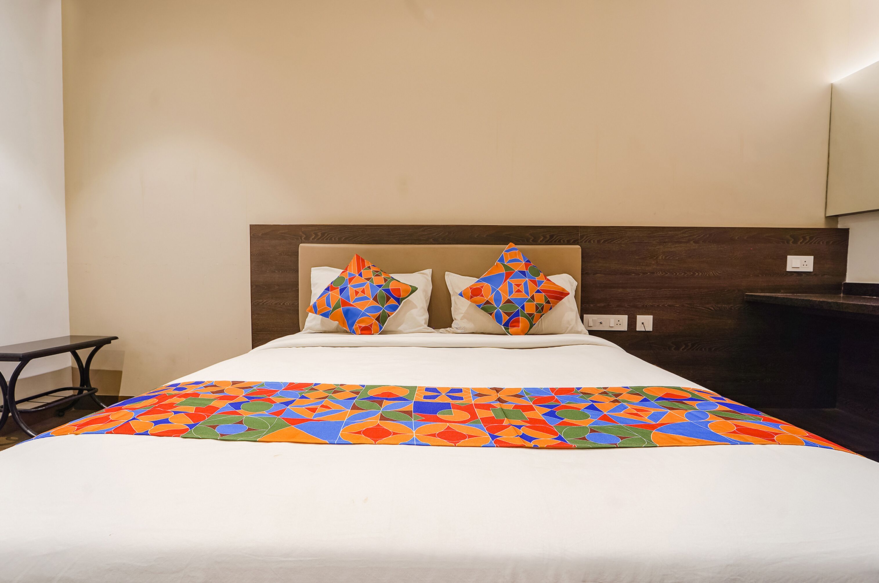 Una habitación de hotel con una cama, dos almohadas, una mesita de noche y un mueble auxiliar.