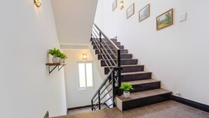Una escalera con barandilla, un estante con plantas y cuadros enmarcados.