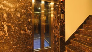 An elevator with glass doors, a marble wall, and a staircase with a marble finish. - Fabhotel Prime Tiyara Inn (Barasat)