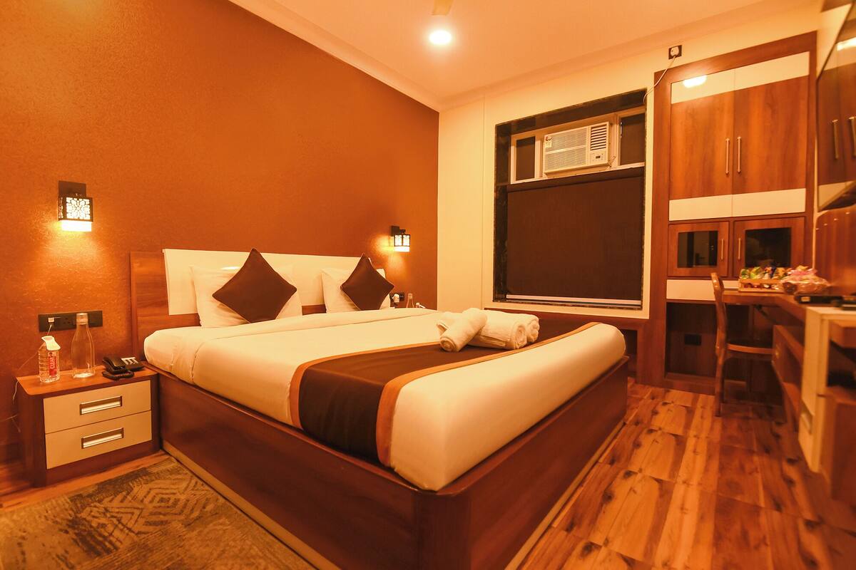 A hotel room with a large bed, bedside tables, a wooden floor, and a kitchenette area.