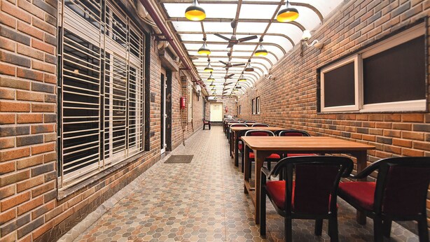 A narrow corridor with brick walls, a tiled floor, and multiple tables and chairs arranged along the sides. - Fabhotel Prime Tiyara Inn (Barasat)