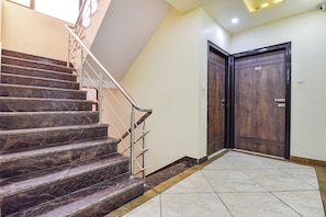 Uma escadaria com corrimão de metal que leva a um patamar, uma porta de madeira e um chão de azulejos.