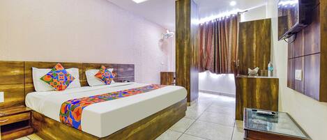 Una habitación de hotel con cabecera de madera, cama con almohadas de diseños geométricos coloridos, una mesita de centro de vidrio y un televisor montado en la pared.