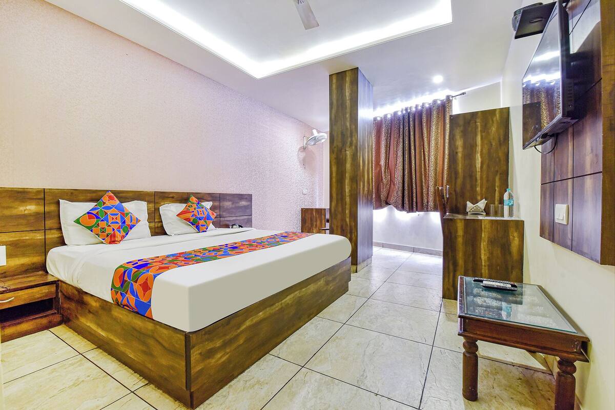 Habitación de hotel con cama de madera, una mesita de cristal, televisor y baño con ducha y cortinas.