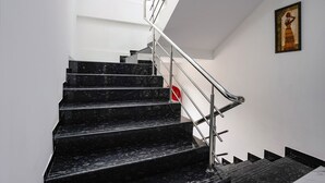 A staircase with black marble steps and a metal railing, leading to a landing with a red fire alarm. - Fabhotel Fortuna Inn (Navi Mumbai)