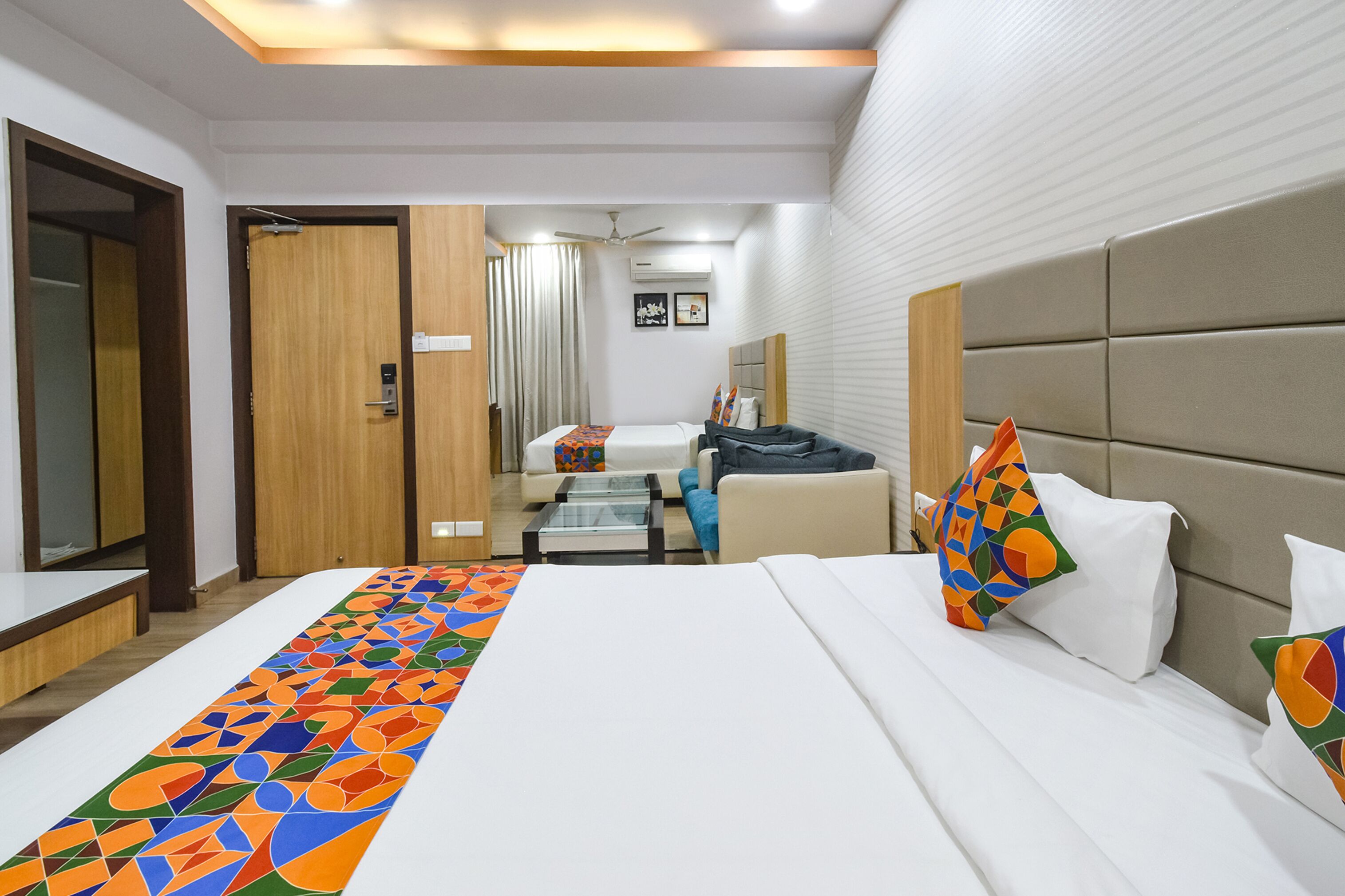 A hotel room with a large bed, a sofa, a small table, and a ceiling fan.