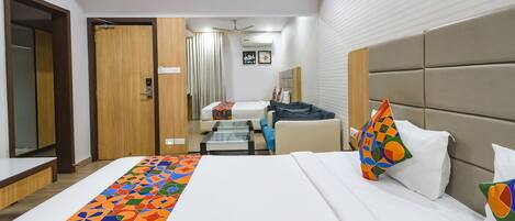 A hotel room with a large bed, a sofa, a small table, and a ceiling fan.