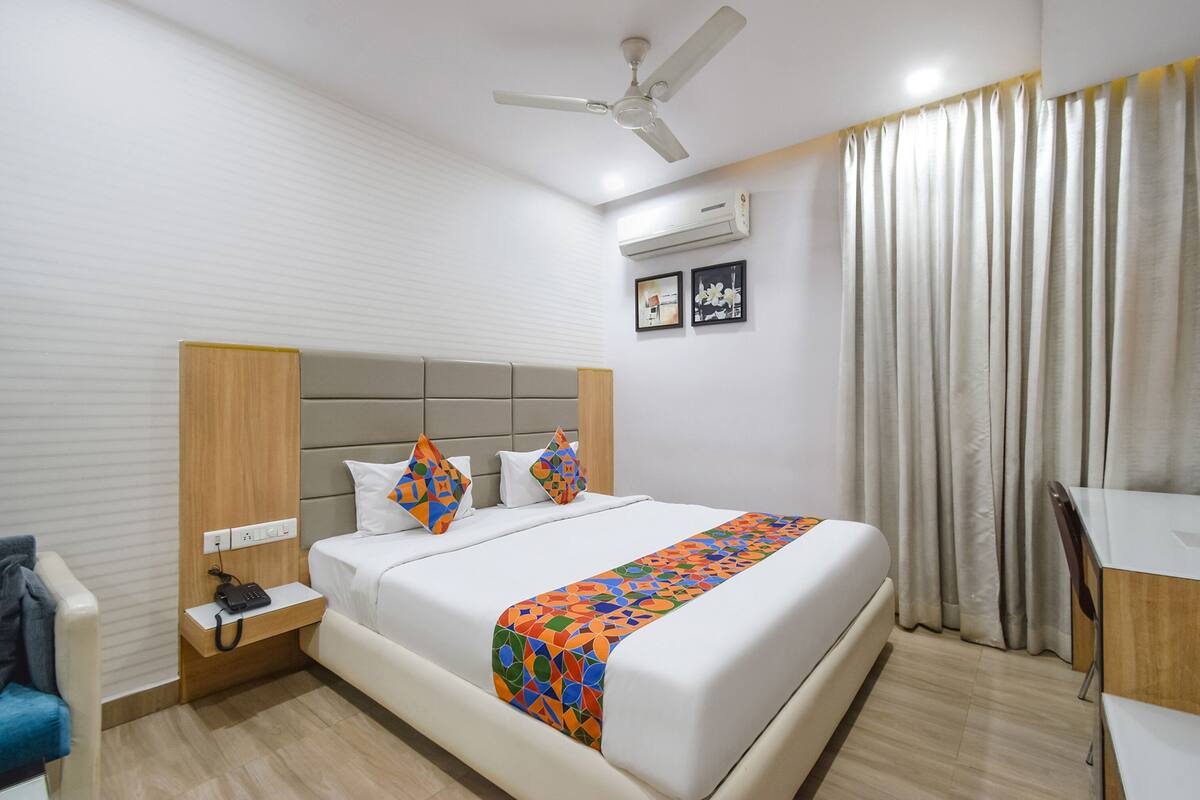 Quarto de hotel com cama, escrivaninha, cadeira, ventoinha no teto e ar condicionado.