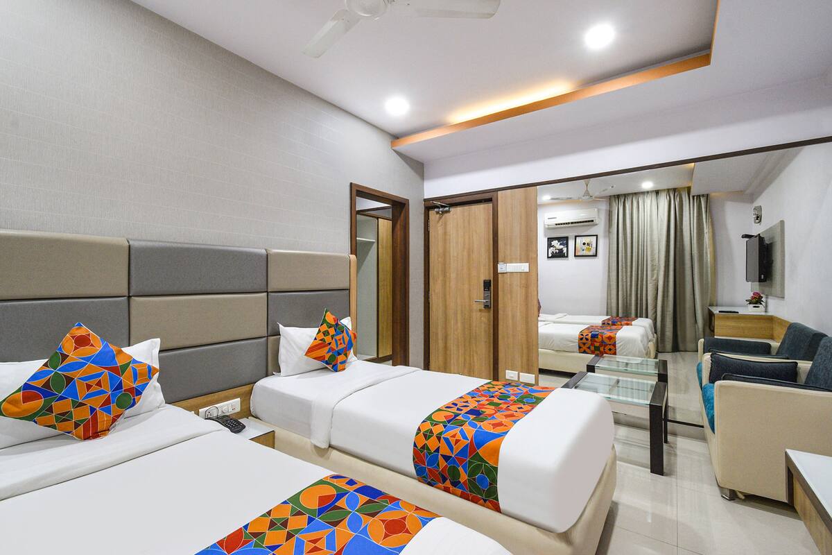 Quarto de hotel com duas camas, um sofá, uma televisão e um ventilador de teto.