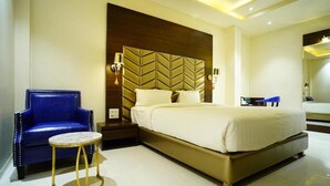 A hotel room with a large bed, a blue armchair, a small round table, and a decorative headboard. - Fabhotel Prime Orange Tree (Nagpur)
