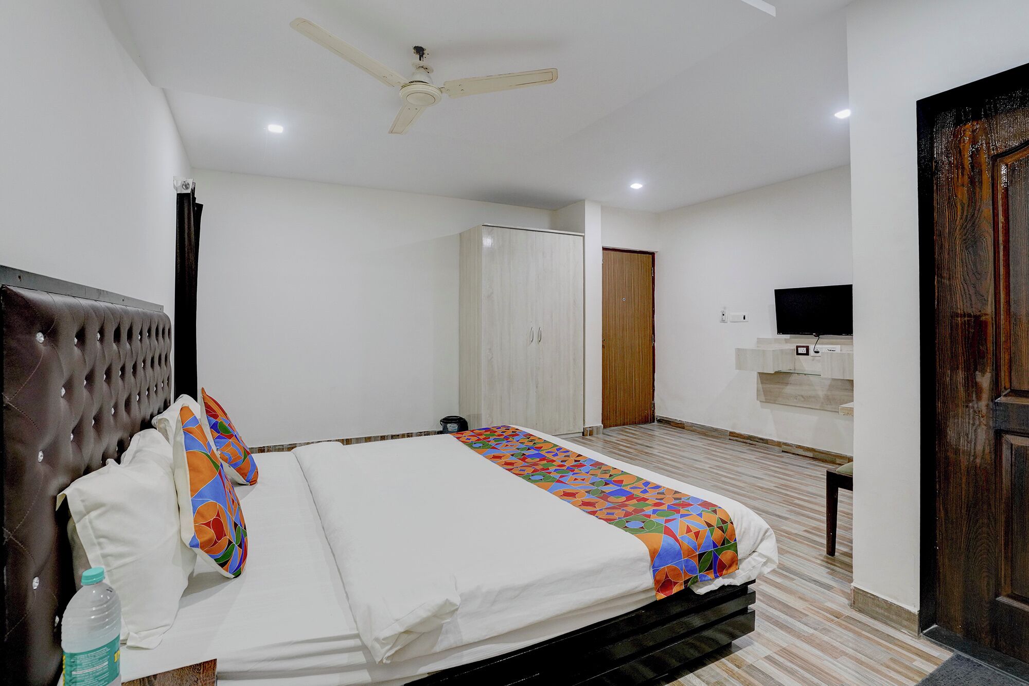 A bedroom with a bed, a ceiling fan, a wardrobe, a television, and a door.