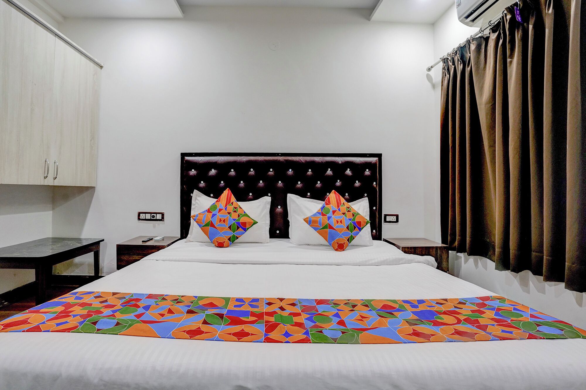 A hotel room with a bed, a nightstand, a wardrobe, and a window with curtains.