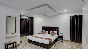 A modern bedroom with a large bed, a bedside table, a nightstand, a ceiling fan, and a window with curtains. - FabHotel The Sky - Nr. Calangute Beach (Calangute)