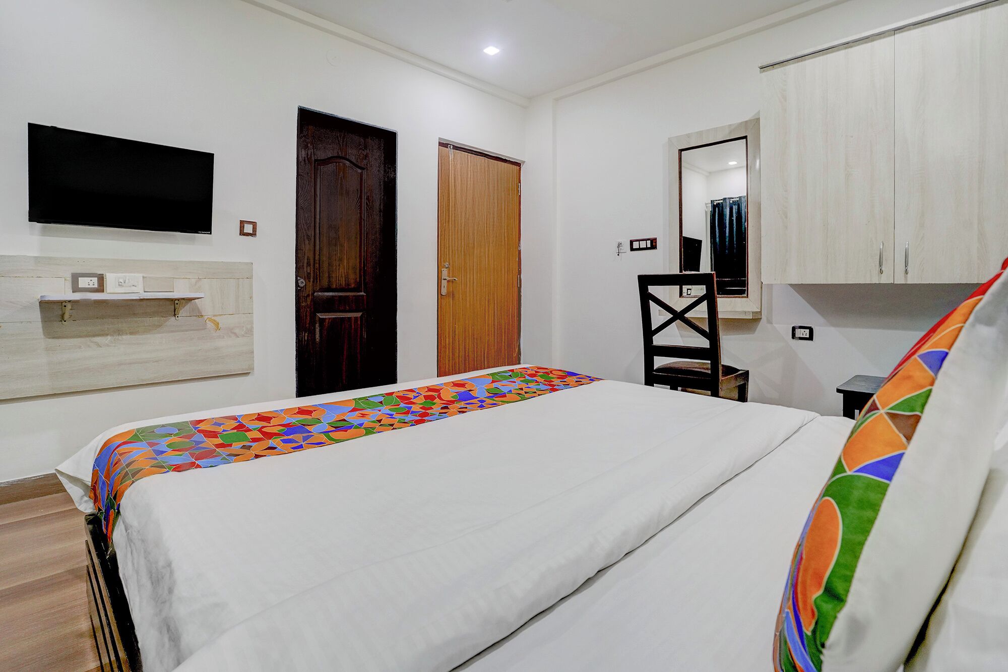 Une chambre à coucher avec un lit, un téléviseur fixé au mur, une porte en bois et une armoire.