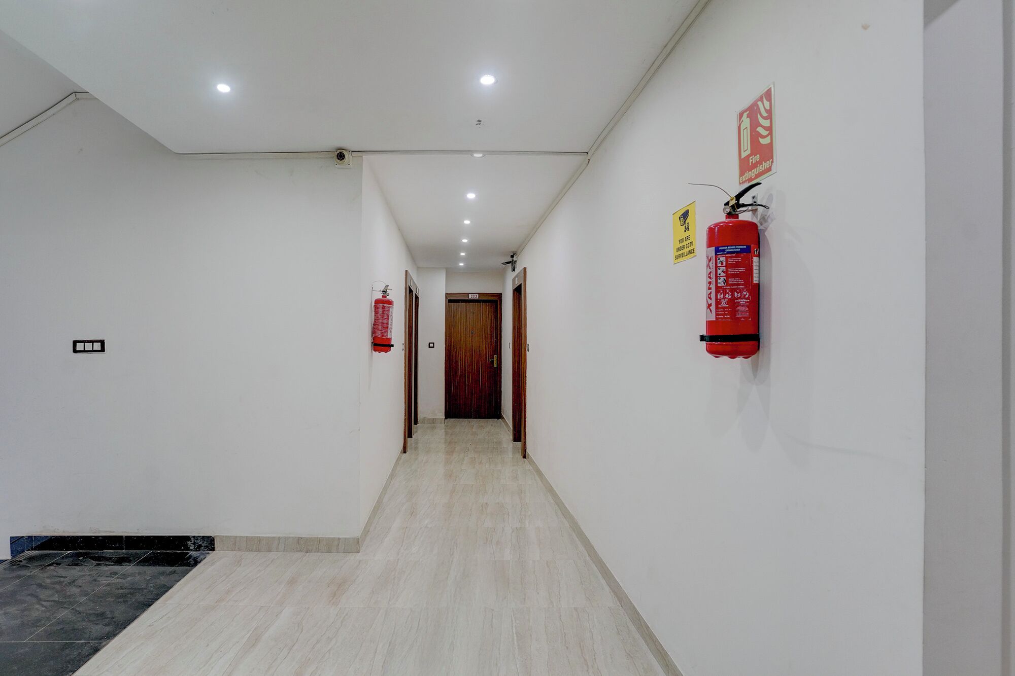 Ein Flur mit weißen Wänden, einem gefliesten Boden und zwei roten Feuerlöschern an der Wand.