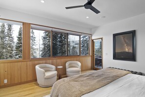 A bedroom with a large window, a bed, two chairs, and a ceiling fan.