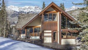 Un chalet moderne doté de grandes fenêtres, d’un revêtement extérieur en bois et offrant une vue sur des montagnes enneigées.