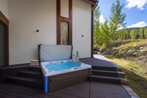 A hot tub on a wooden deck with steps leading up to it, surrounded by a natural landscape.