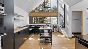 Une cuisine moderne avec un plan de travail en bois, des meubles noirs et une grande fenêtre donnant sur des arbres couverts de neige.