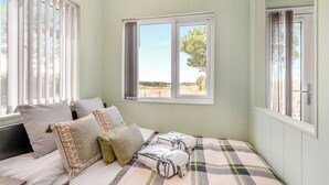 Une chambre à coucher avec un lit, des oreillers, une couverture et une fenêtre donnant sur l’extérieur.