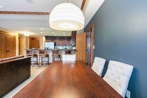 Eine moderne Küche mit Holzausbau, einer zentralen Kochinsel und einem Essbereich mit großem Holztisch und weißen Polstersesseln.