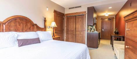 A bedroom with a large bed, wooden wardrobe, and a desk with a lamp.