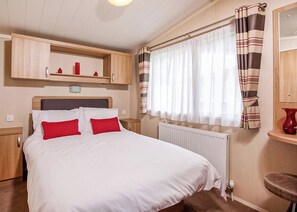 Une chambre à coucher avec un lit, un radiateur, une fenêtre avec des rideaux, une étagère avec des objets et une chaise.