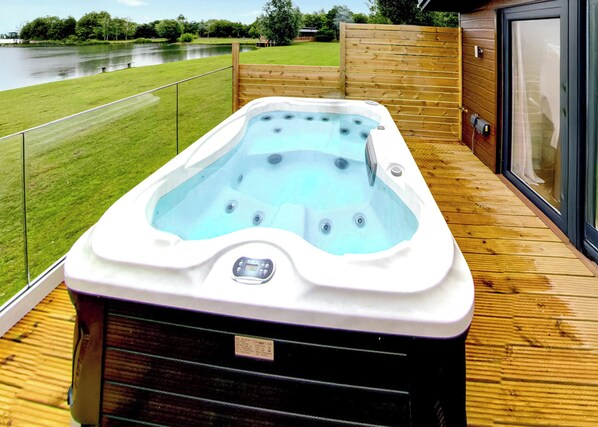 A hot tub on a wooden deck with a view of a lake.