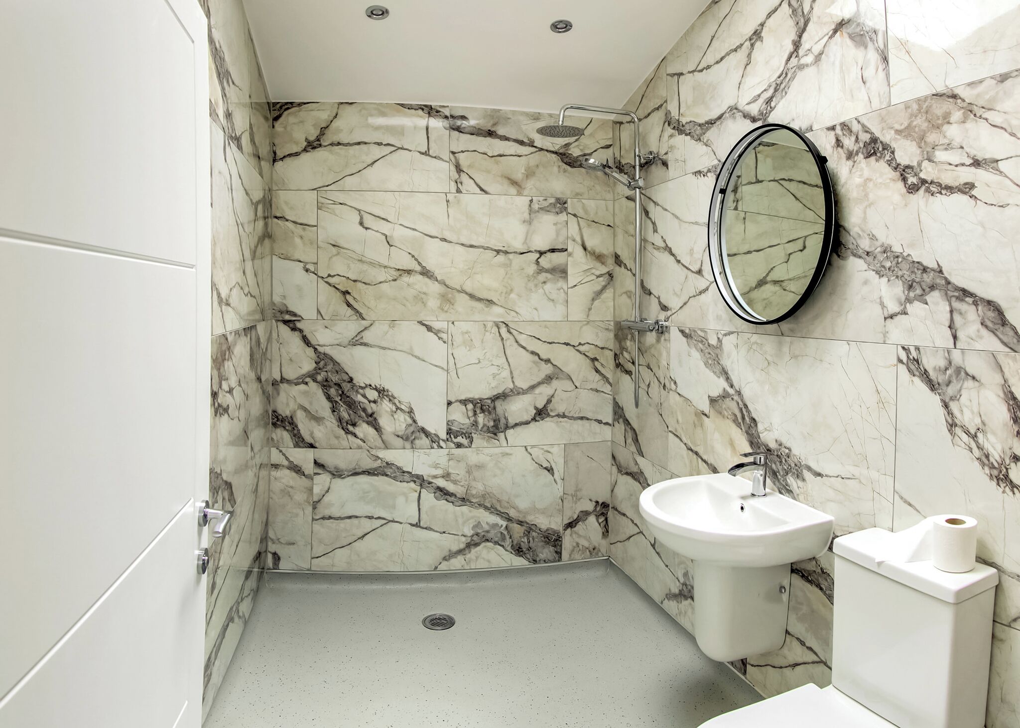 Een badkamer met marmeren wanden, een douche, een wastafel en een toilet.