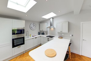 A modern kitchen with white cabinetry, a built-in oven, a microwave, a sink, and a large island with a cutting board.