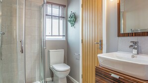 A bathroom with a glass shower enclosure, a toilet, a wooden door, and a sink with a mirror. - The Watchtower (Pet) (Snowdonia)