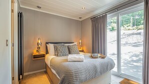 A bedroom with a large bed, bedside lamps, a window with curtains, and a view of the outdoors. - The Watchtower (Pet) (Snowdonia)