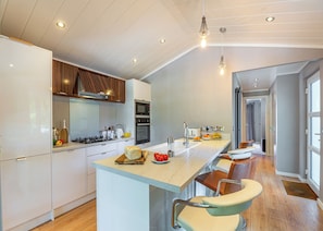 A modern kitchen with a central island, stainless steel appliances, and a view to the adjacent living area. - The Watchtower (Pet) (Snowdonia)