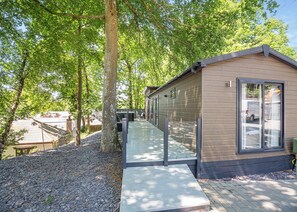 A modern wooden cabin with a glass door, surrounded by trees and a gravel path.