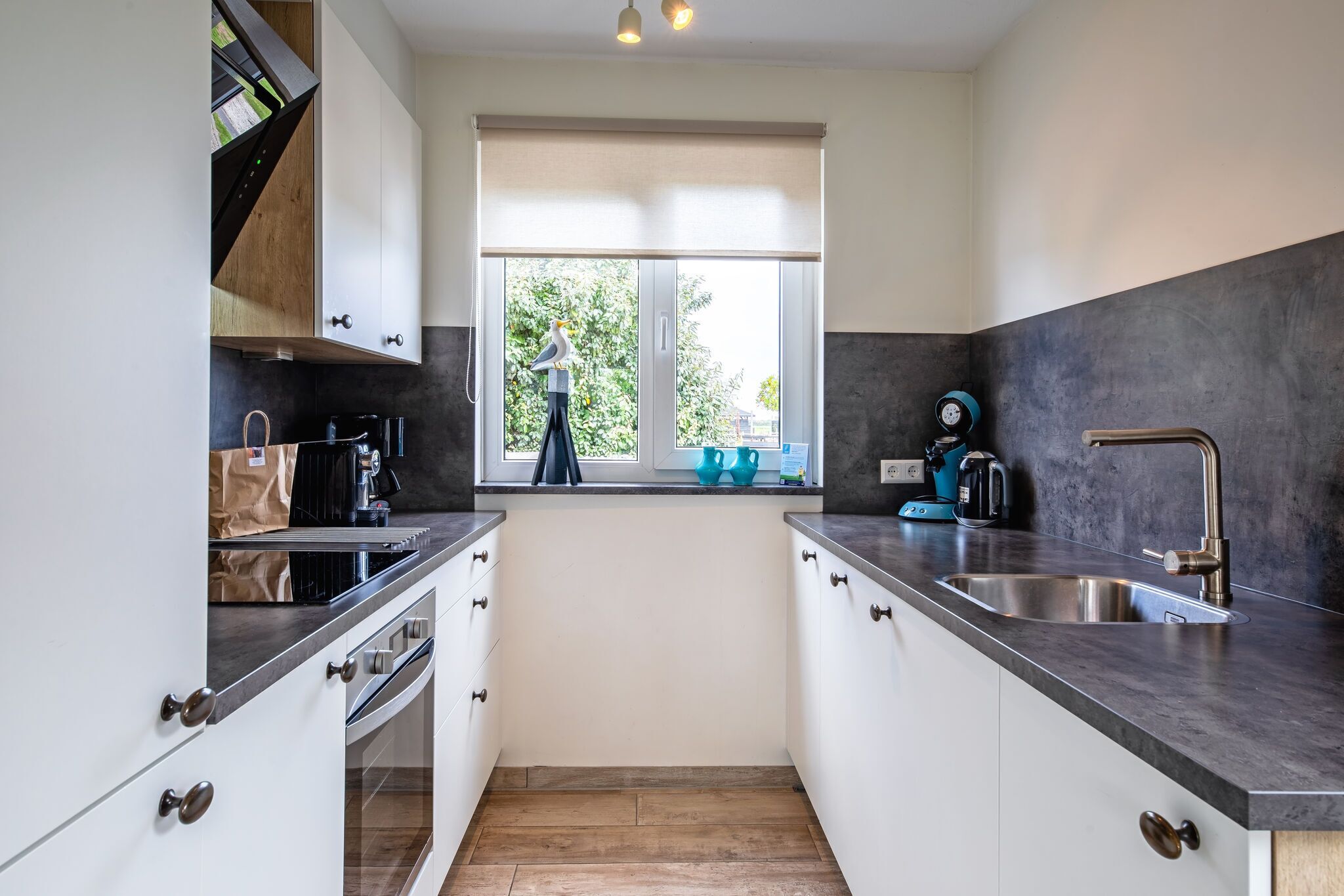 Cocina moderna con armarios blancos, encimera negra y ventana con vistas a zonas verdes.