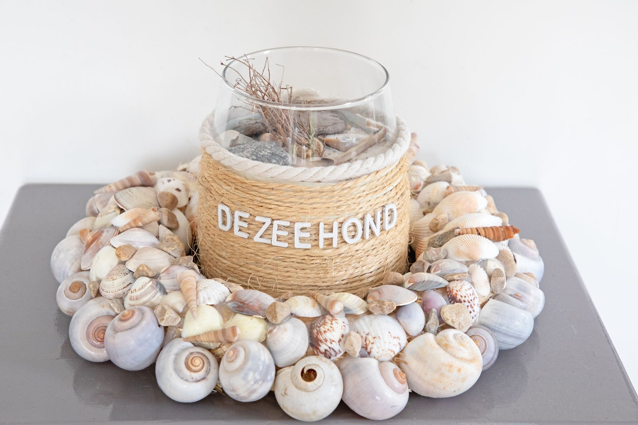 Een decoratieve glazen vaas met de tekst 'DEZEEHOND' omringd door schelpen.