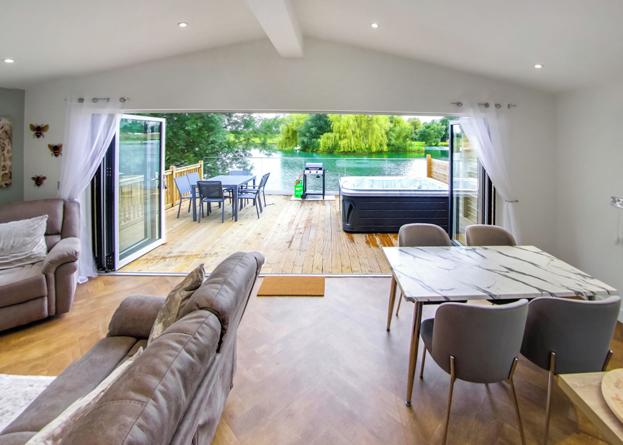 Een moderne woonkamer met een bank, eettafel en stoelen, een bubbelbad en uitzicht op een meer door grote glazen deuren.