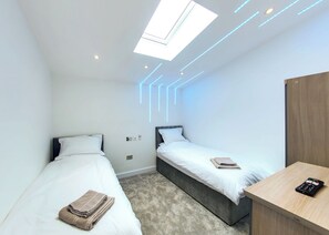 Quarto de hotel moderno com duas camas, um claraboia e uma mesa com painel de controle.
