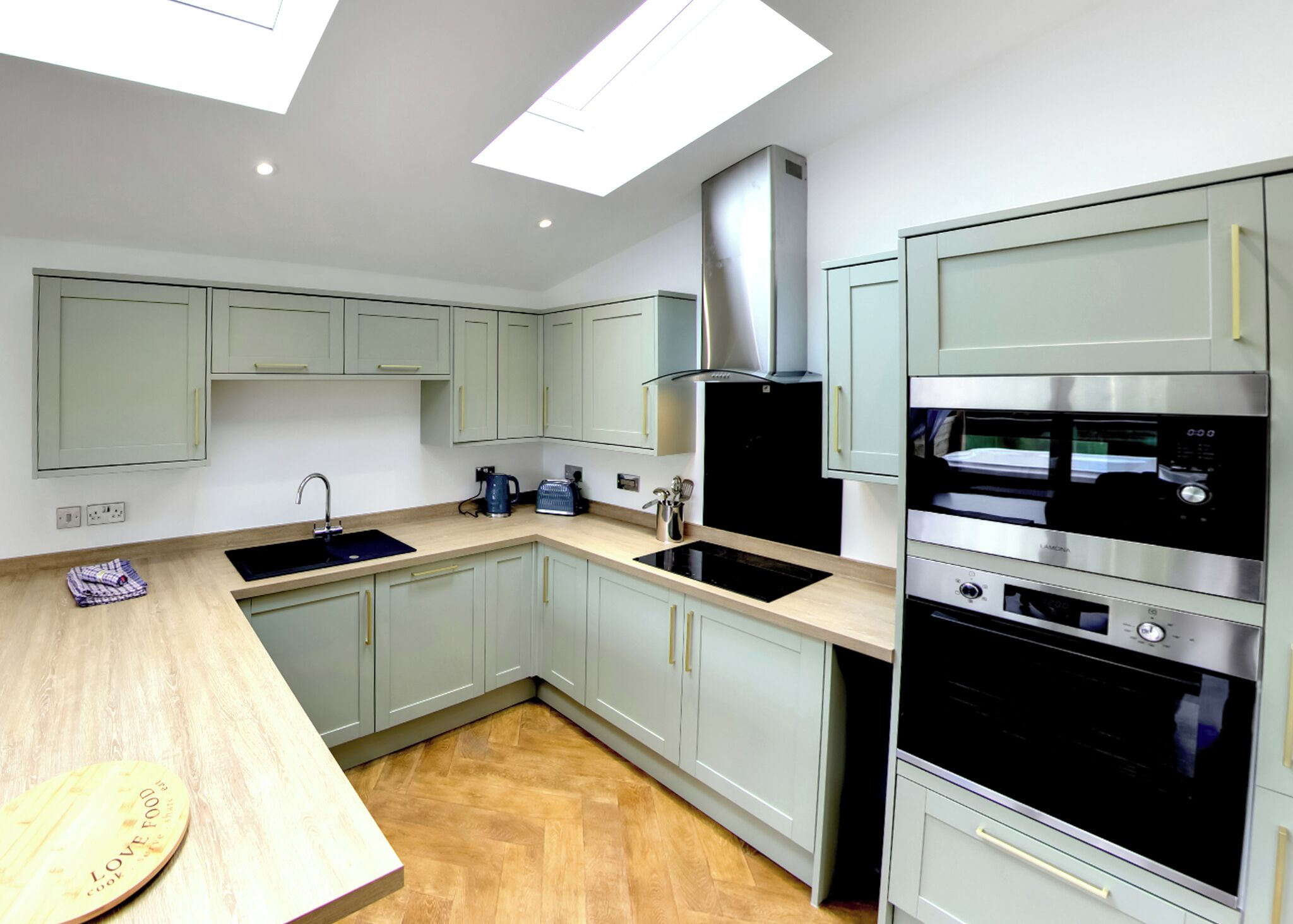 A modern kitchen with light green cabinets, a black stove, and a wooden countertop.