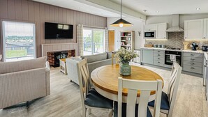 Una sala moderna con chimenea, un comedor con una mesa redonda y una cocina con armarios grises.